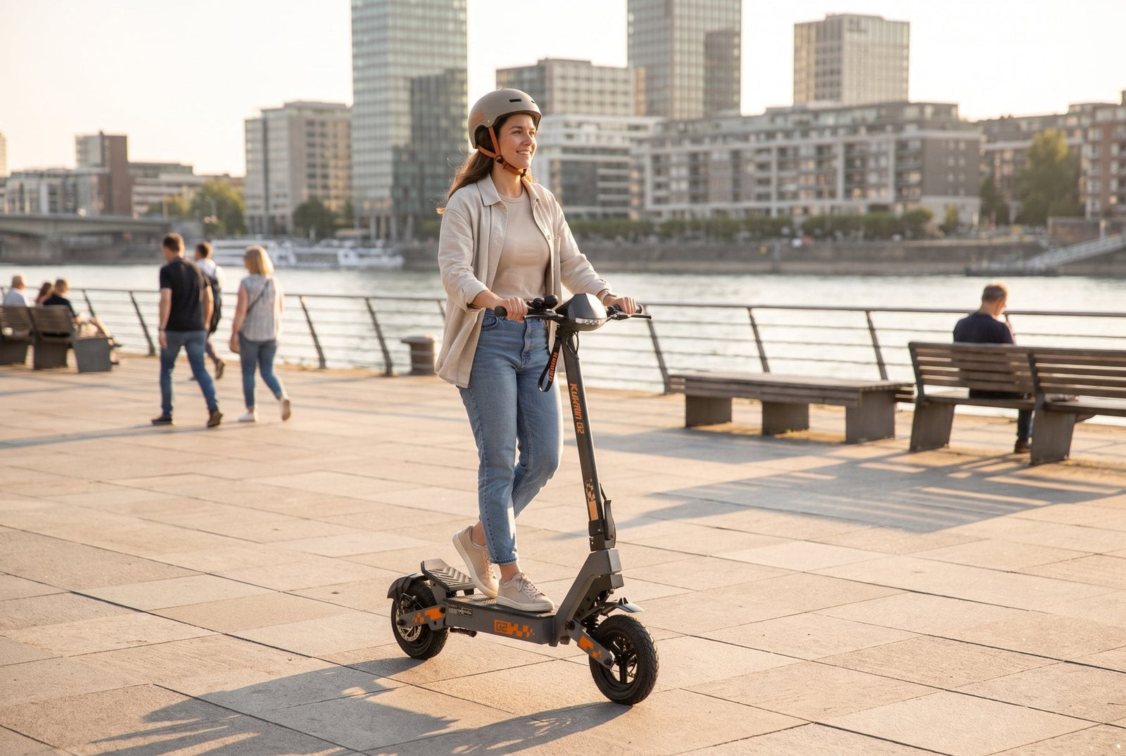 Woman in a helmet riding a KuKirin G2 electric scooter along a riverside promenade