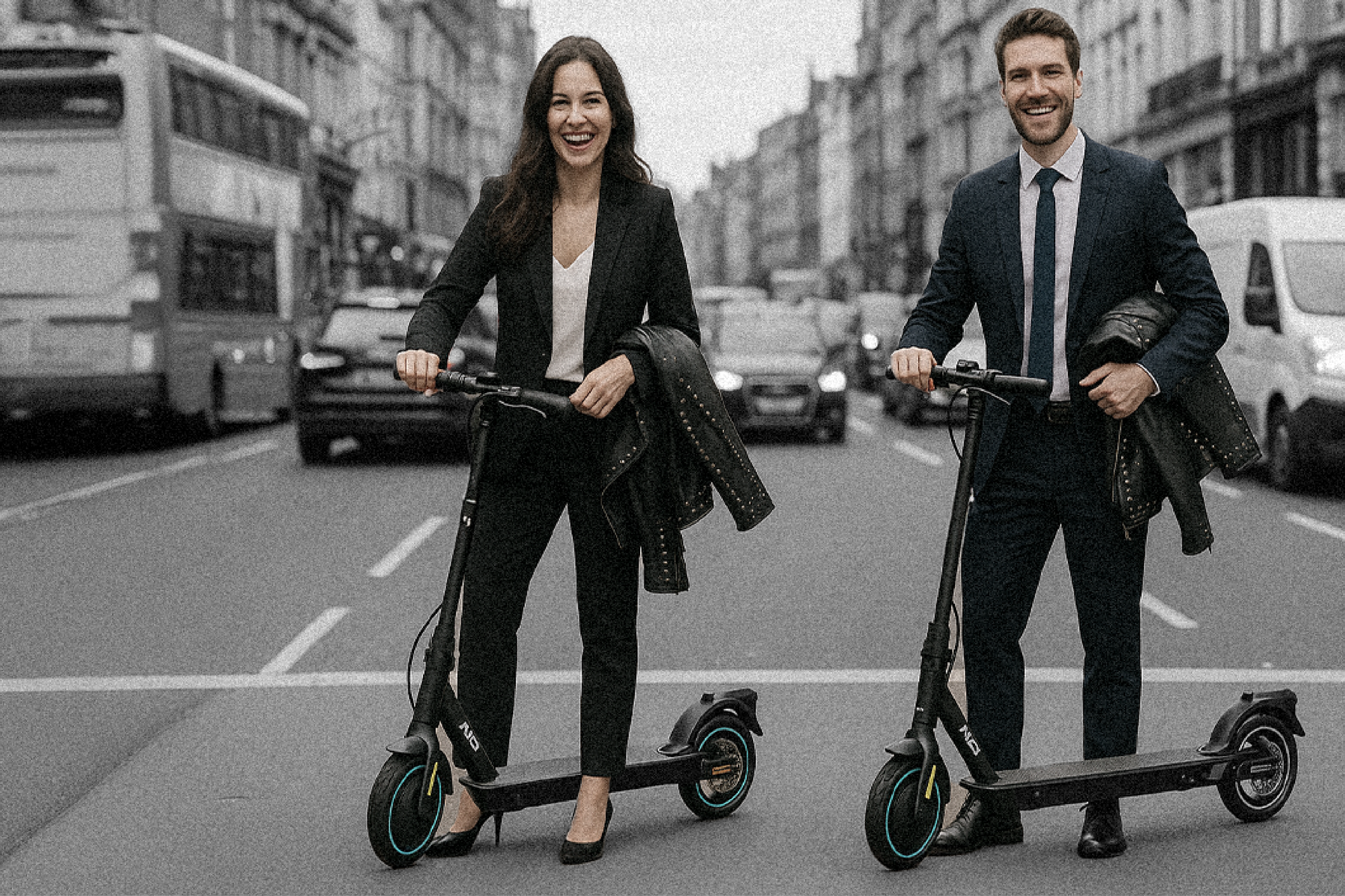 Two people riding electric scooters on a city street with buildings and vehicles in the background.